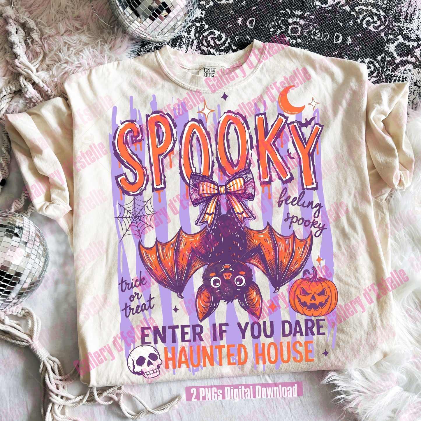 A cream-colored graphic t-shirt featuring a Halloween design with a bat, the word 'SPOOKY' in orange, and other decorative halloween illustrations, laid flat on a white faux fur surface with decorative props.