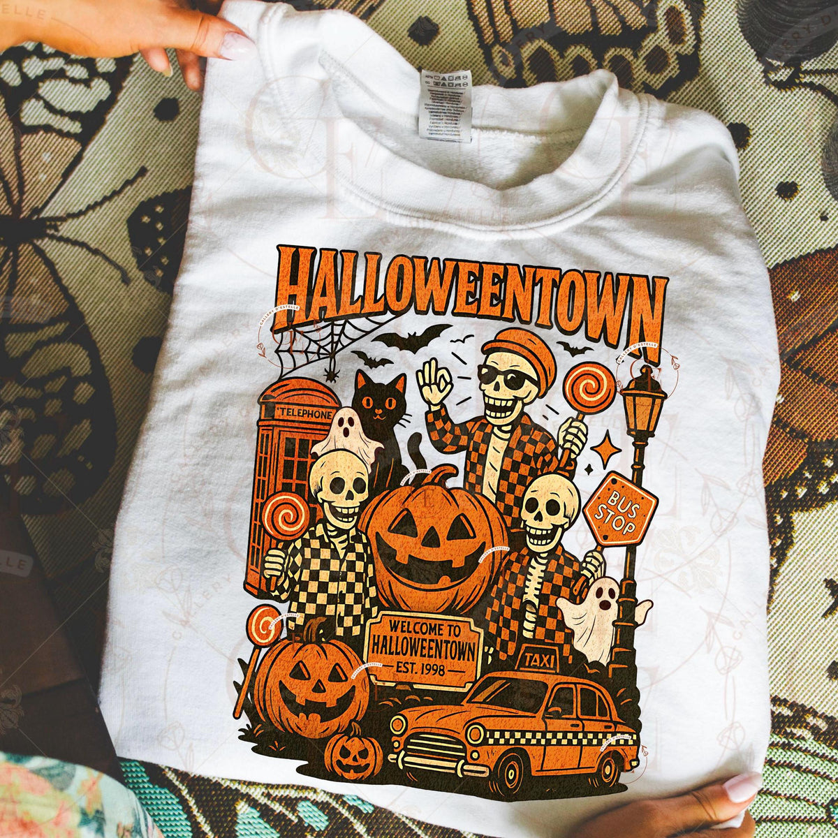 White t-shirt with 'Halloweentown' graphic design featuring skeletons, pumpkins, and a taxi.