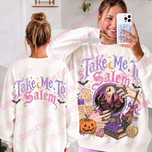 A woman modeling a white sweatshirt with a 'Take Me To Salem' Halloween graphic, showing both the front and back views. The graphic features purple text, a witch in a cauldron, a pumpkin, books, and bats.